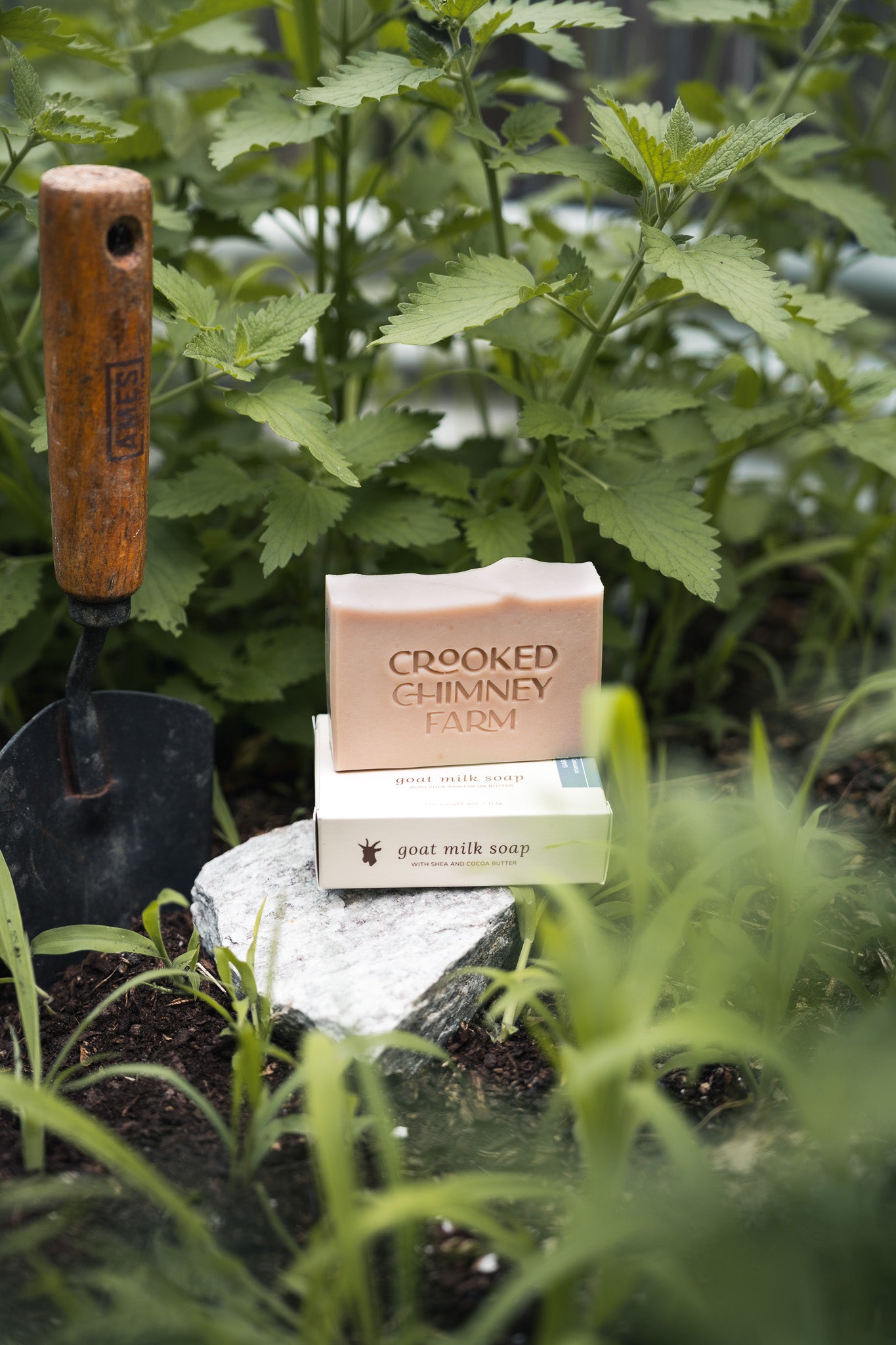 a bar of crooked chimney farm garden soap on a rock in a garden with a trowel