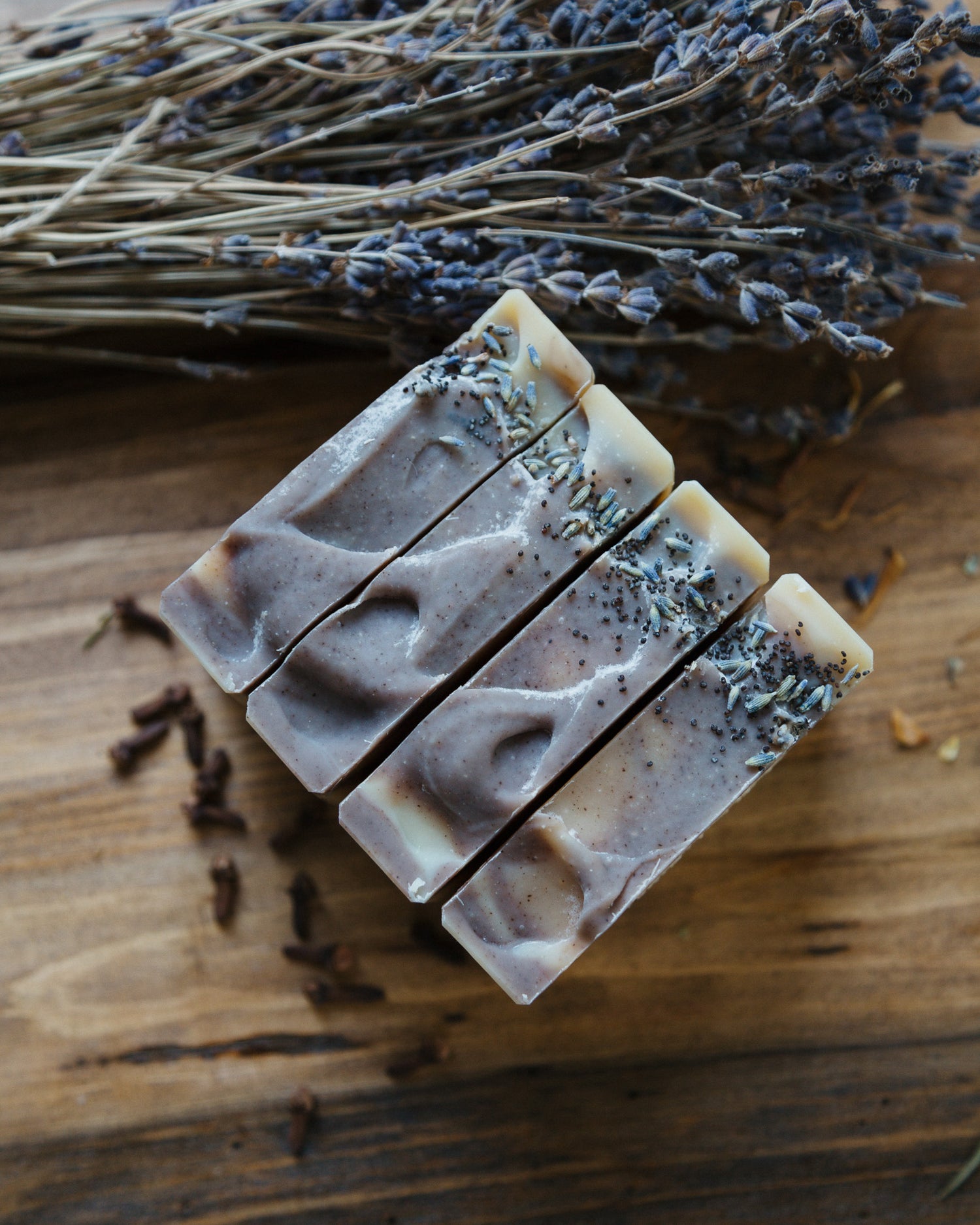 lavender clove soap with purple clay on wood table next to a bundle of lavender