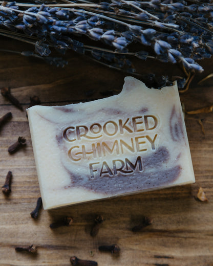 lavender clove soap with purple clay on wood table next to a bundle of lavender