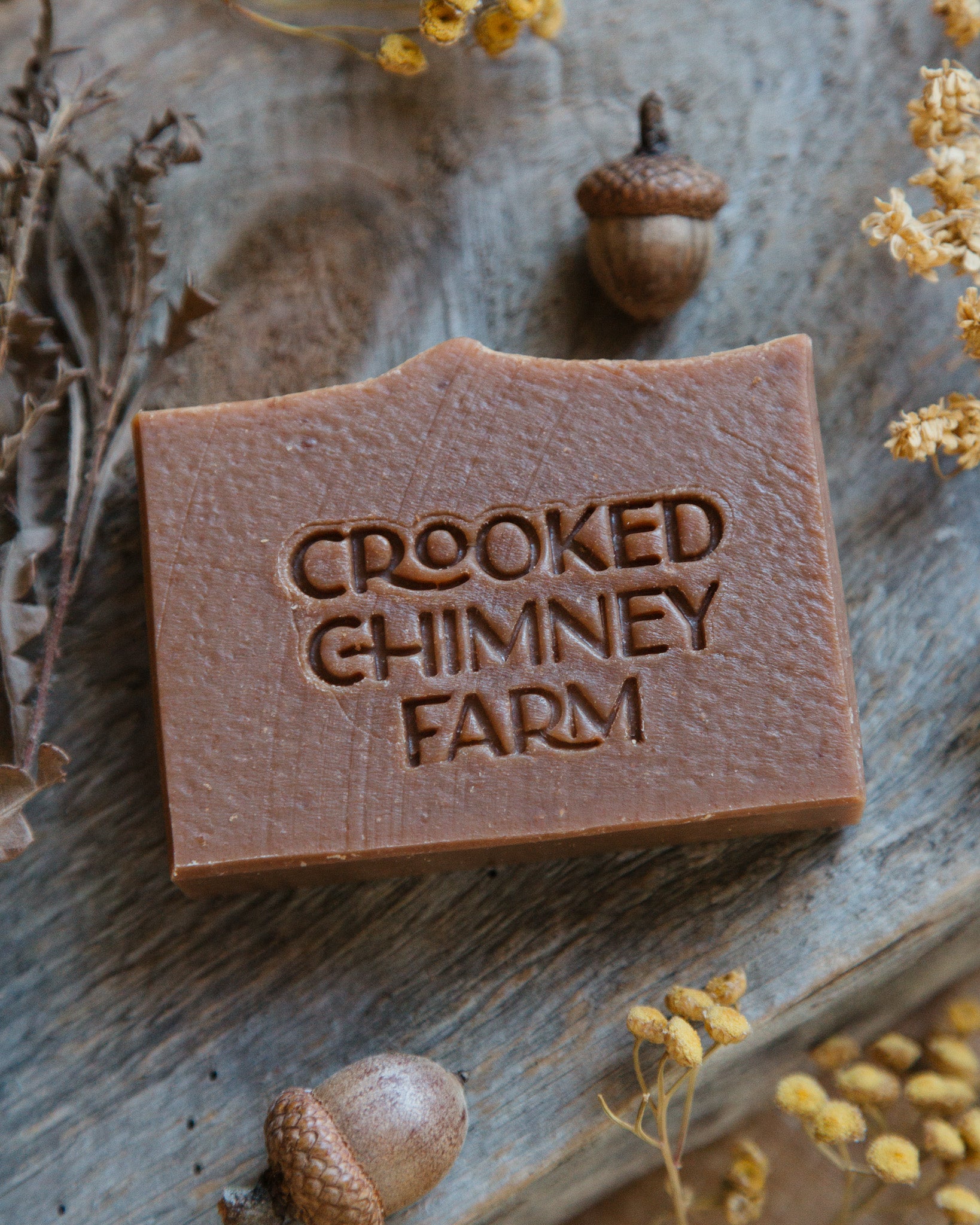 toasted pumpkin goat milk soap on wood plank with dried flowers and acorns 